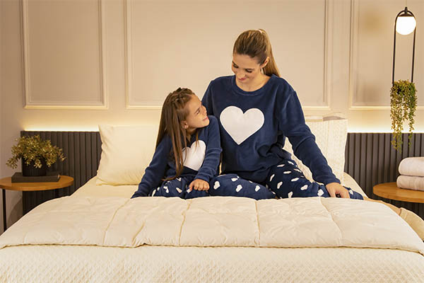 Mulher e criança em cima da cama com pijama appel home